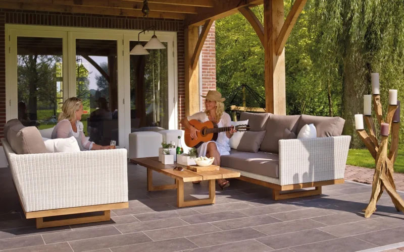 Teak outdoor dining set with honey-brown finish on a stone patio