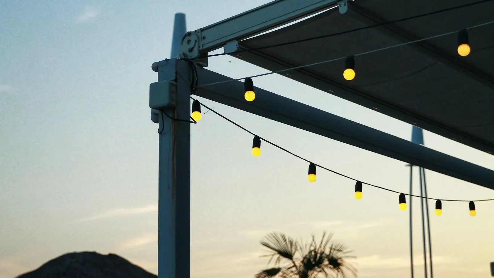 Warm white LED string lights draped across a patio pergola above a wooden seating area at dusk