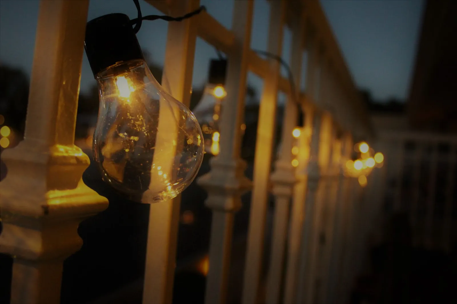 Warm white LED string lights draped across a patio pergola above a wooden seating area at dusk