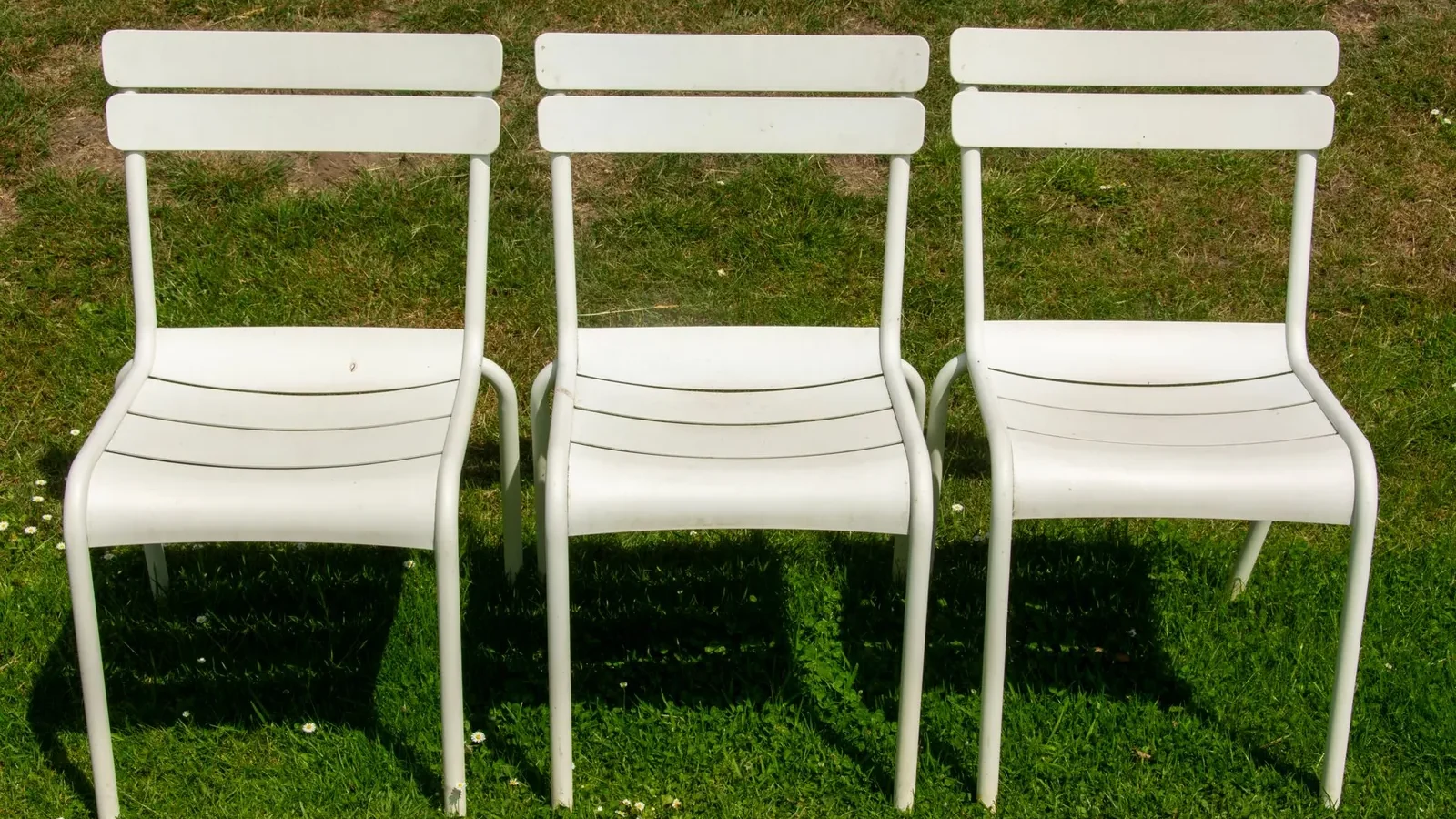 Outdoor dining chairs in teak, aluminum, and wicker styles arranged around a patio table