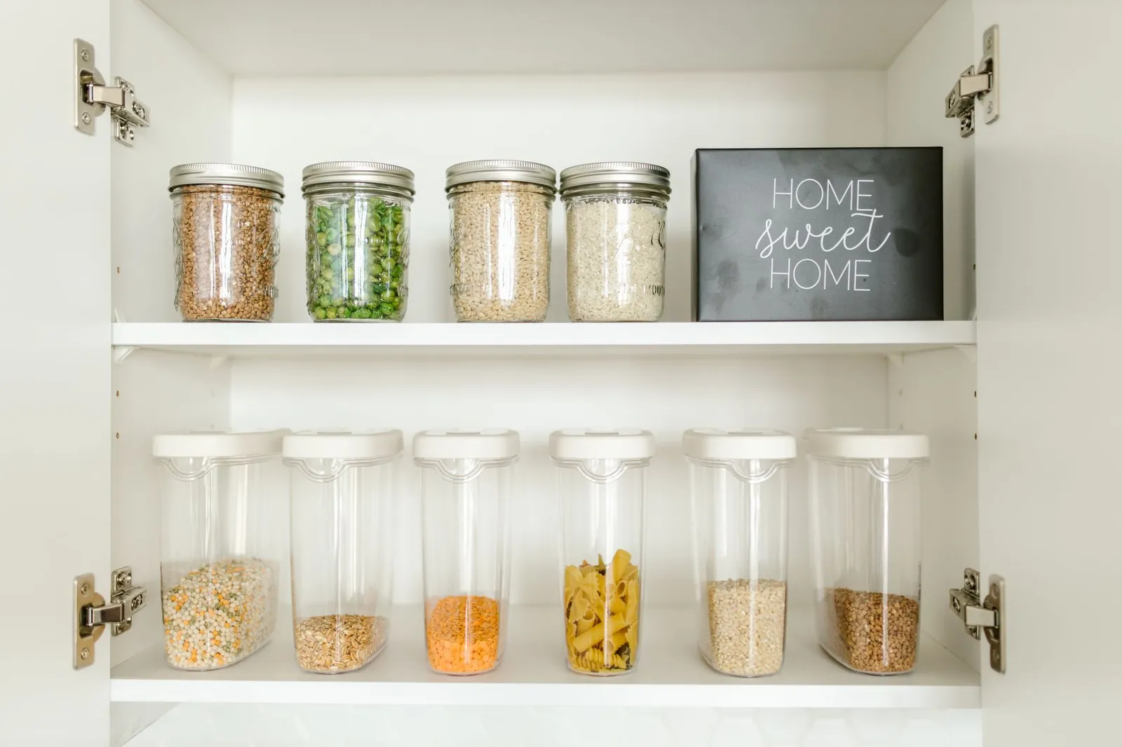 Pantry shelf organized with labeled glass containers, stainless canisters, and plastic bins grouped by category
