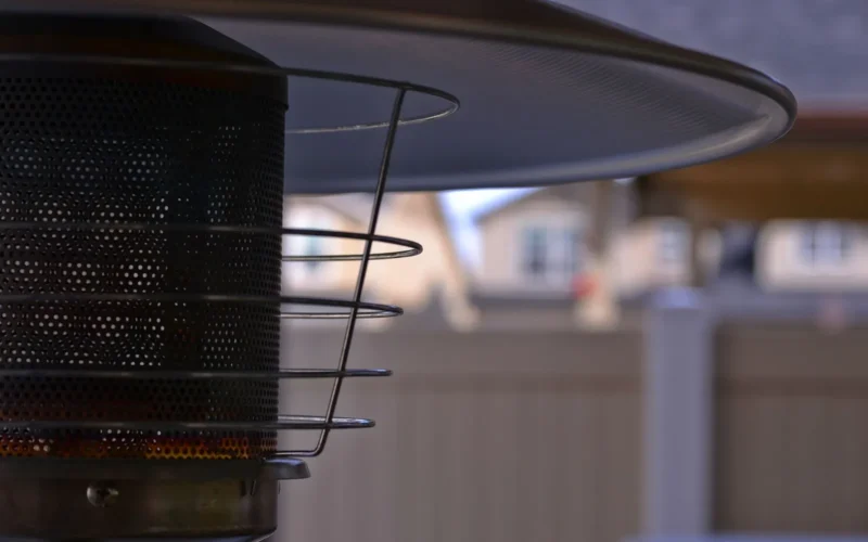 Three types of patio heaters arranged on a small deck: a tabletop propane heater on a side table, a wall-mounted electric heater on the pergola, and a tall pyramid propane heater in the corner