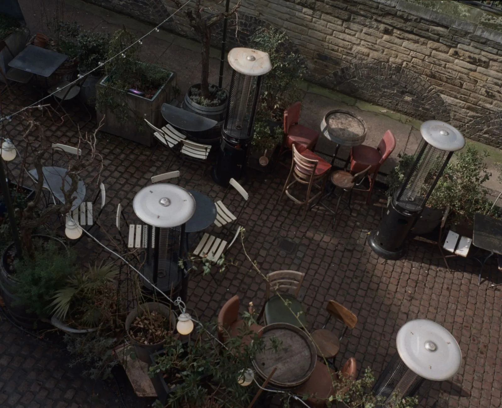 Three types of patio heaters arranged on a small deck: a tabletop propane heater on a side table, a wall-mounted electric heater on the pergola, and a tall pyramid propane heater in the corner