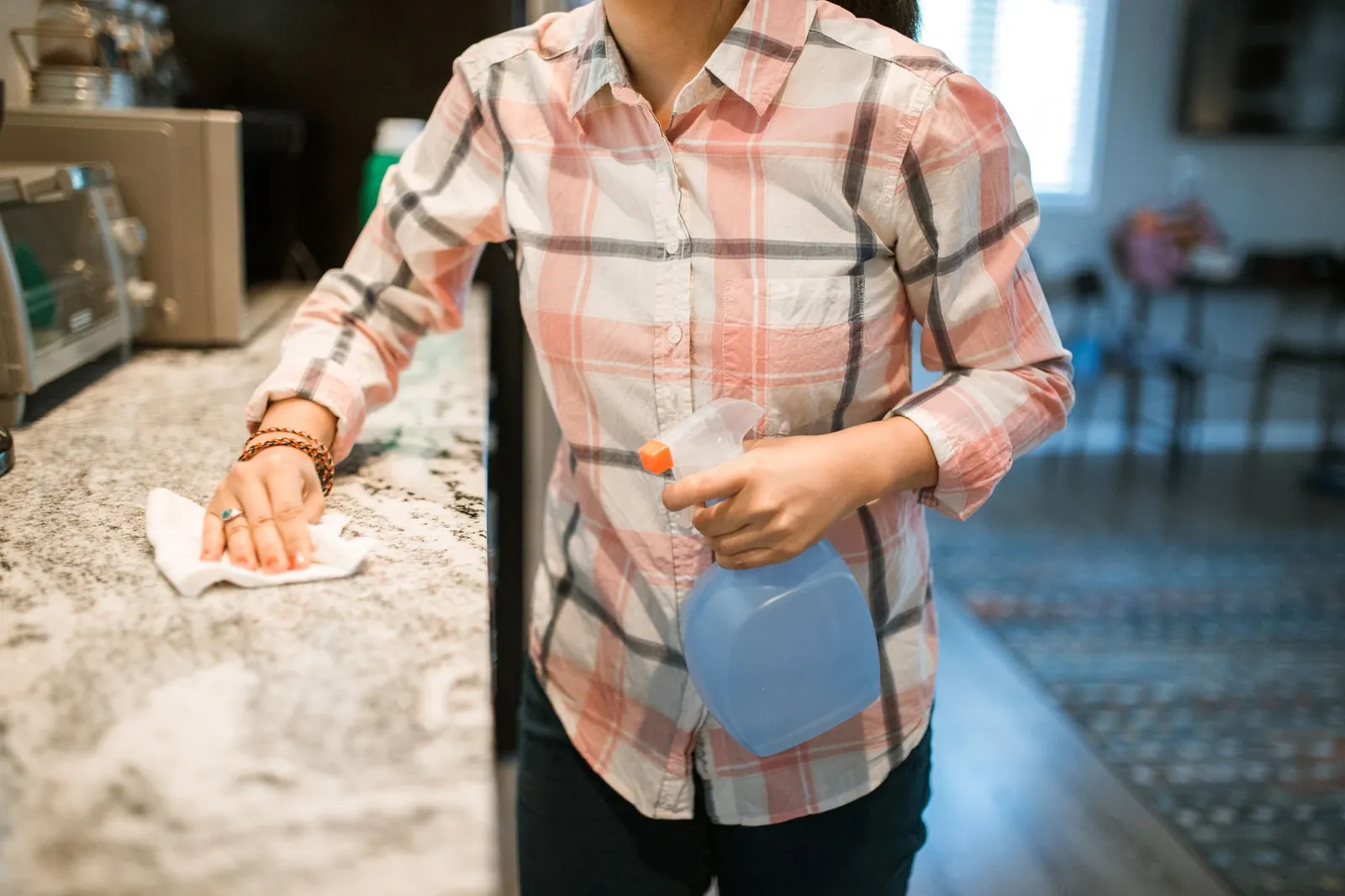 Microfibre cloths, spray bottles, rubber gloves, and a scrub brush arranged on a kitchen counter before a deep clean