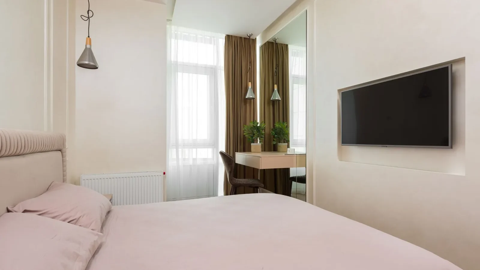 Large wall mirror opposite a bedroom window reflecting natural light into a room with pale walls and minimal furniture