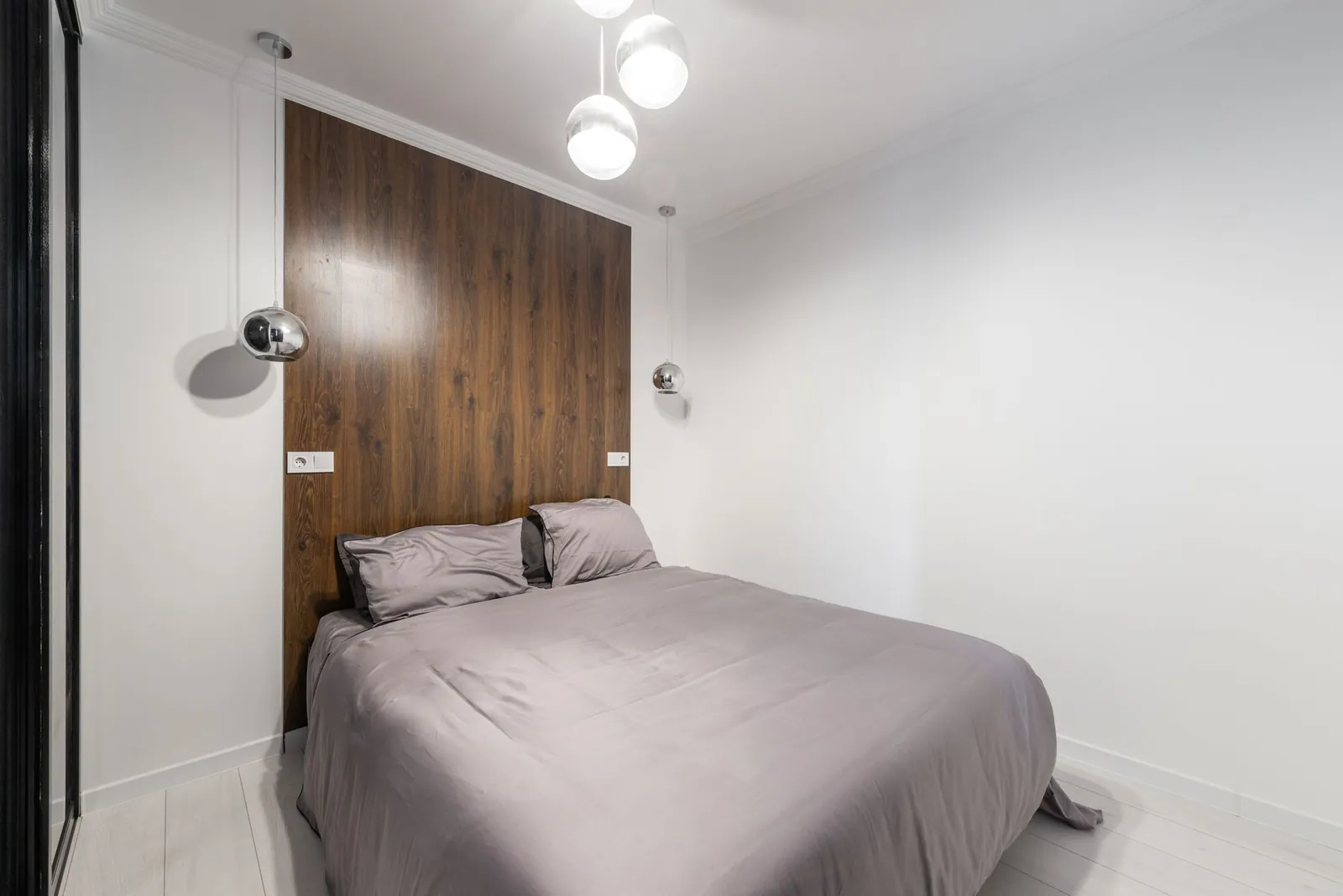 Large wall mirror opposite a bedroom window reflecting natural light into a room with pale walls and minimal furniture