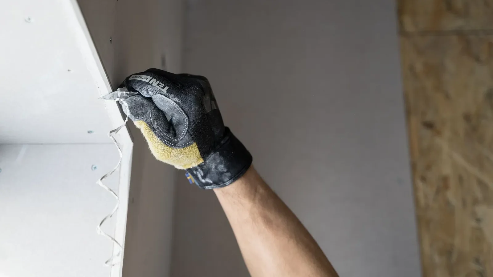 Putty knife and joint compound beside a small nail hole in a painted drywall wall, ready for repair