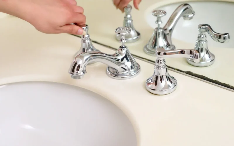 Tap cartridge removed from a single-lever kitchen tap, shown next to the tap body and basic tools including an adjustable wrench and screwdriver
