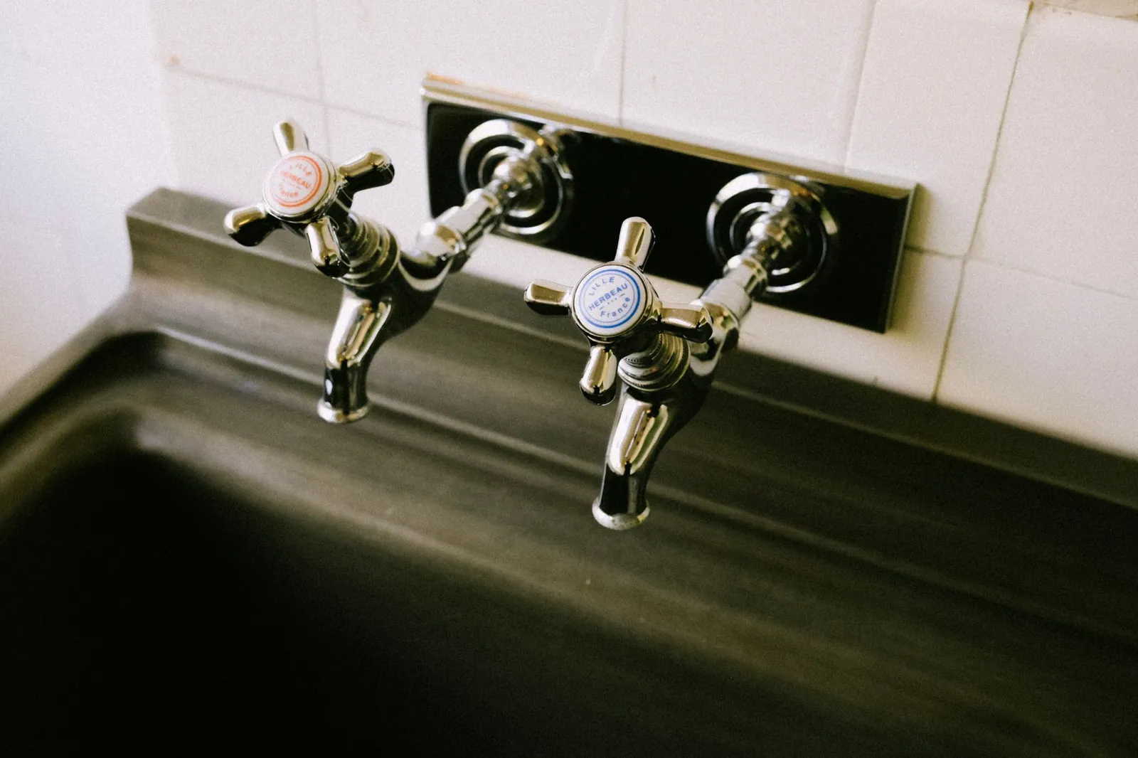 Tap cartridge removed from a single-lever kitchen tap, shown next to the tap body and basic tools including an adjustable wrench and screwdriver