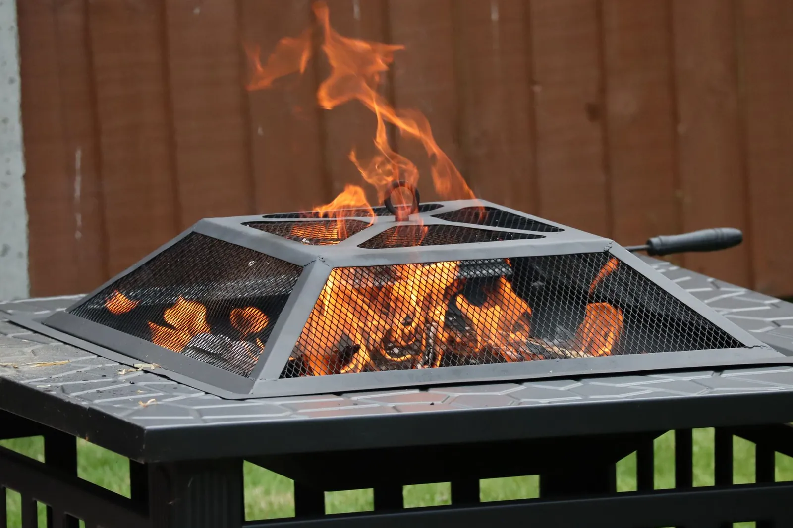 Wood fire pit with open flames surrounded by Adirondack chairs on a backyard lawn