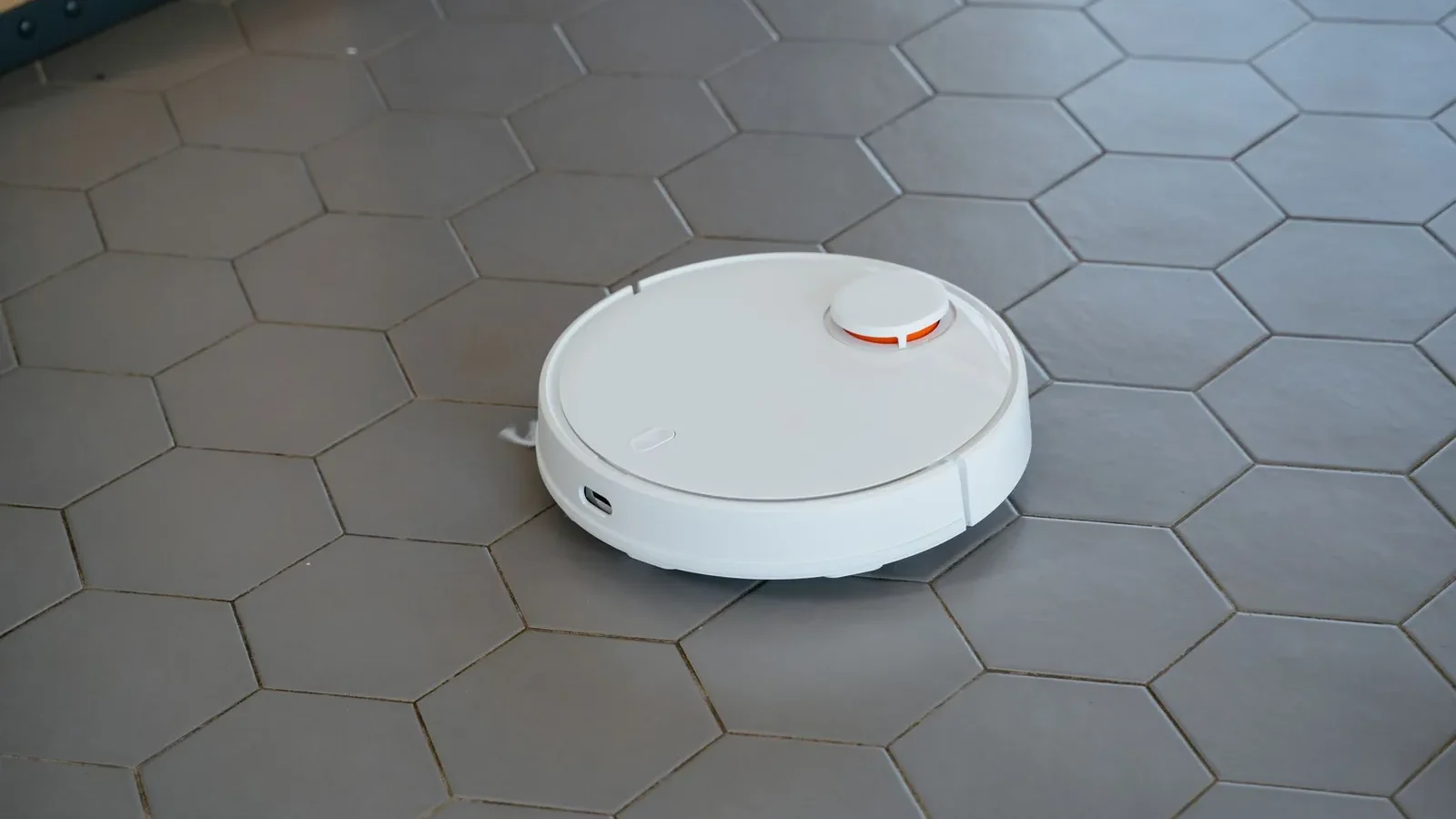 Robot vacuum disc on hardwood floor beside a corded upright vacuum, showing size difference