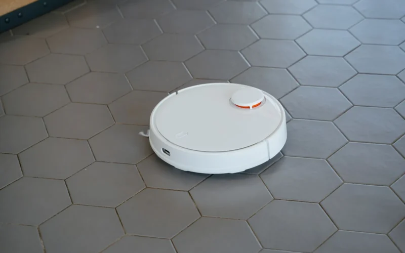 Robot vacuum disc on hardwood floor beside a corded upright vacuum, showing size difference