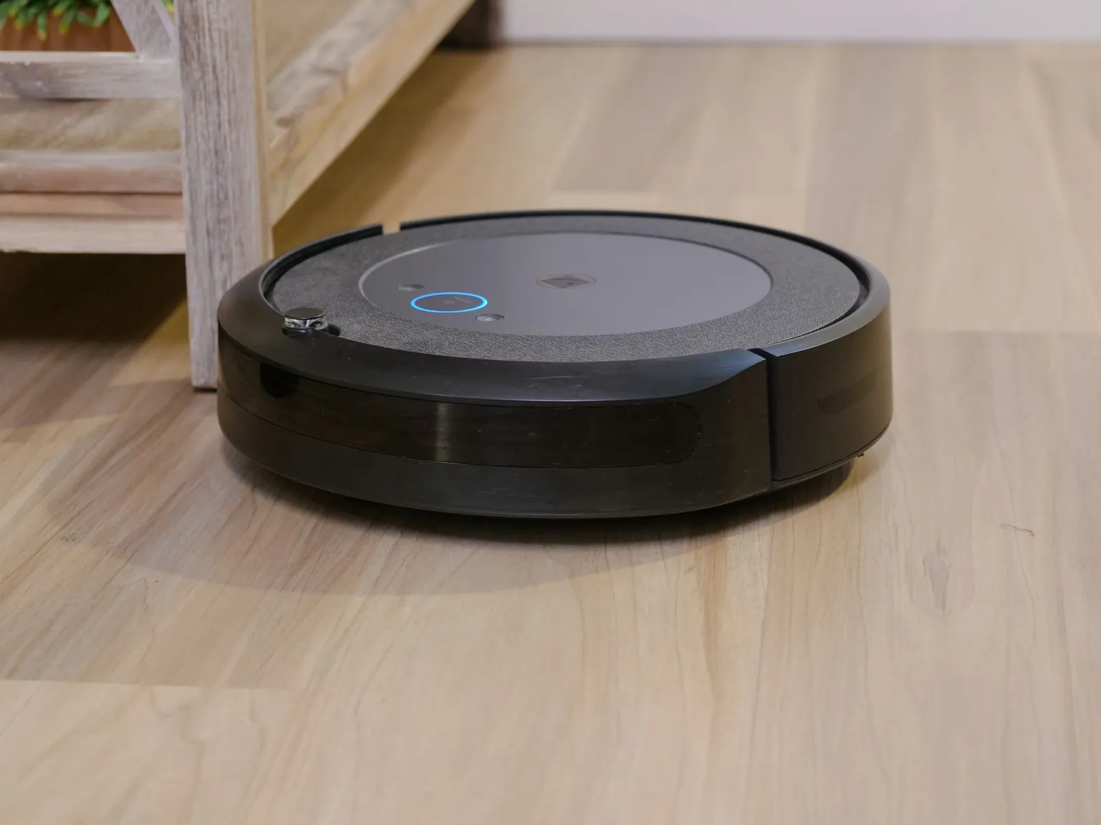 Robot vacuum disc on hardwood floor beside a corded upright vacuum, showing size difference
