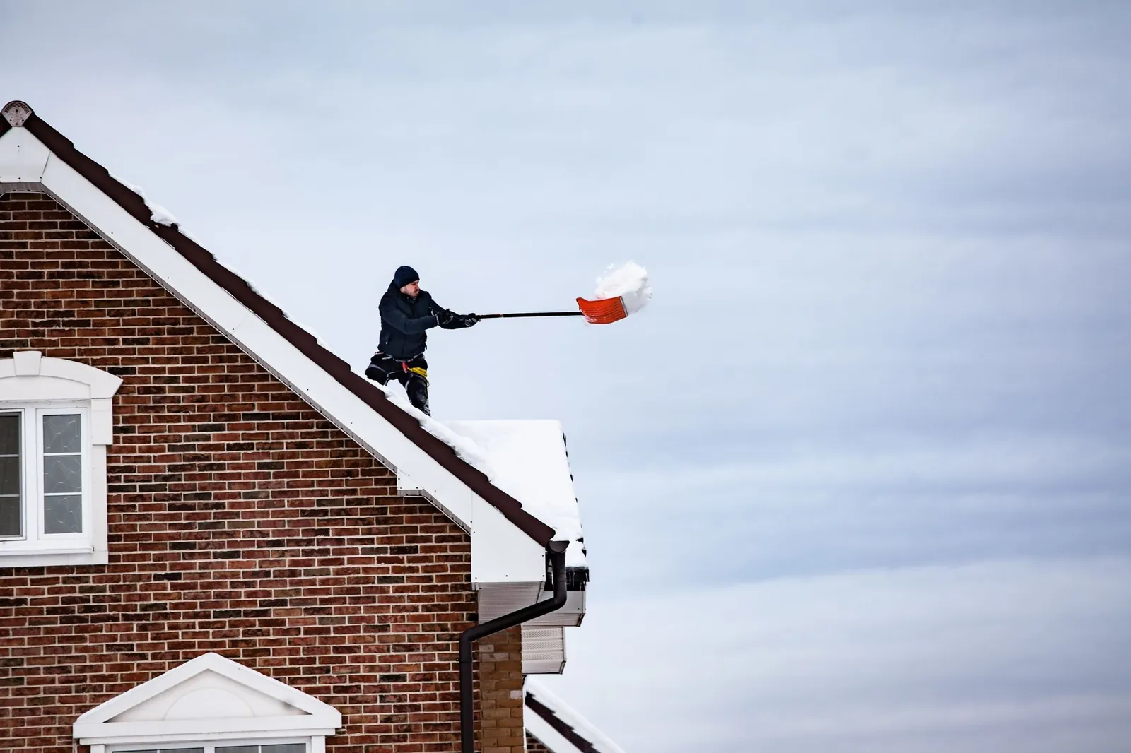Homeowner clearing leaves and shingle granules from a residential gutter in early spring