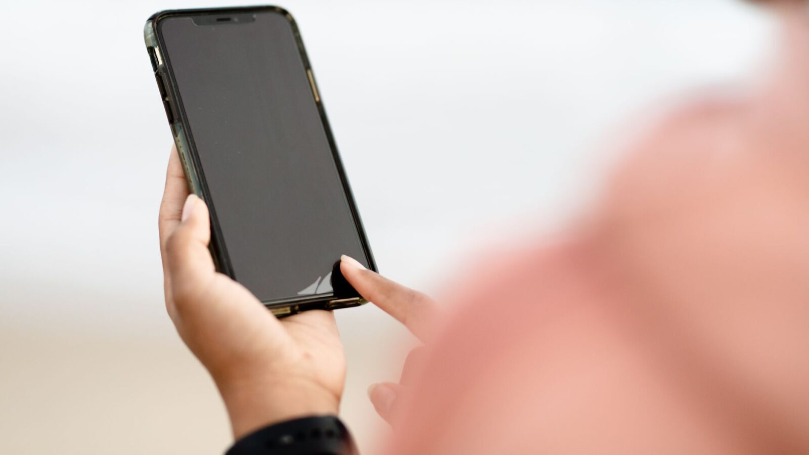 A hand interacting with a smartphone touchscreen outdoors. Modern technology concept.