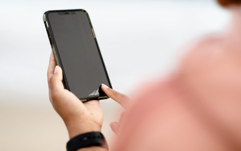 A hand interacting with a smartphone touchscreen outdoors. Modern technology concept.