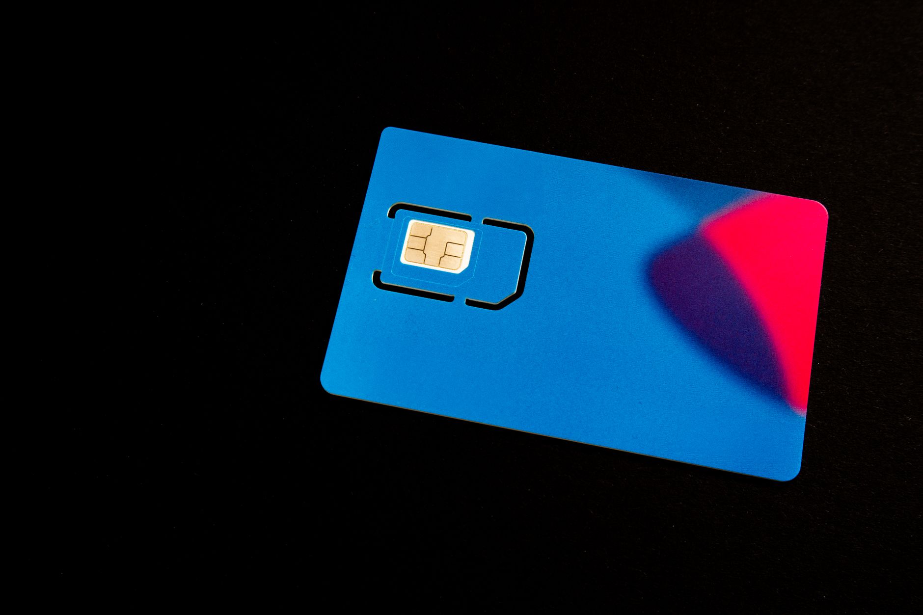 A blue SIM card on a dark background with vibrant red and purple accents.